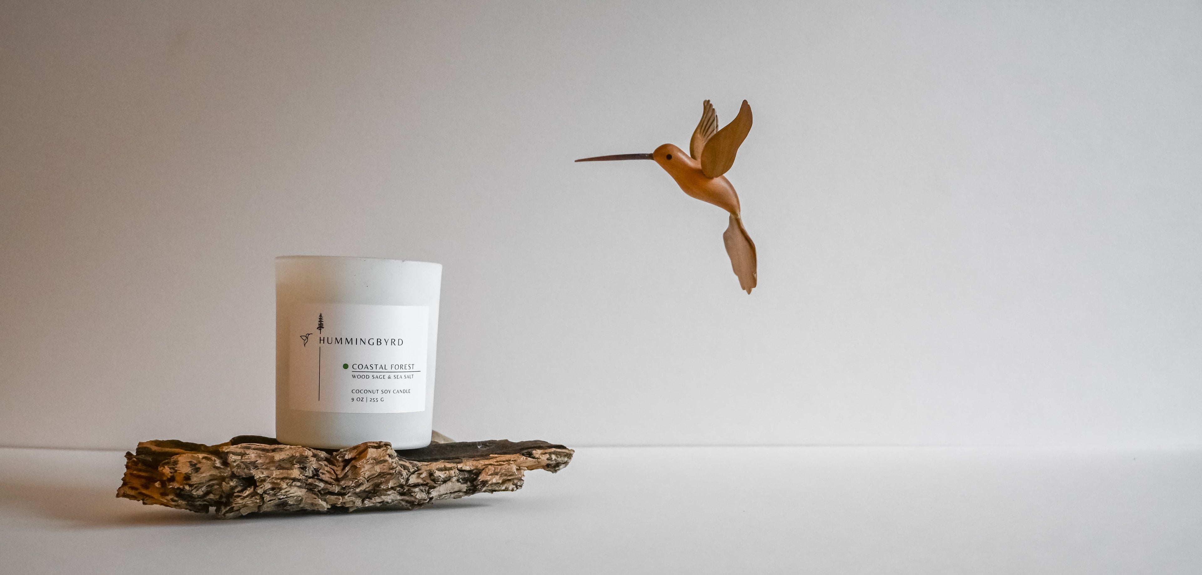 Candle on a piece of driftwood with a small floating wooden hummingbird figurine